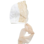 Nanù white baby bonnet with gold macrame lace trim and delicate gold bead embellishments. Features sheer ties.